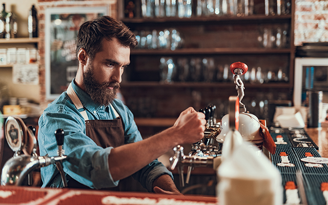 Barkeeper steht hinter der Bar und zapft ein Bier Barkeeper steht hinter der Bar und zapft ein Bier
