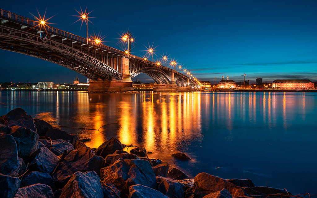 Lichter der Theodor-Heuss-Brücke spiegeln sich bei Nacht im Rhein