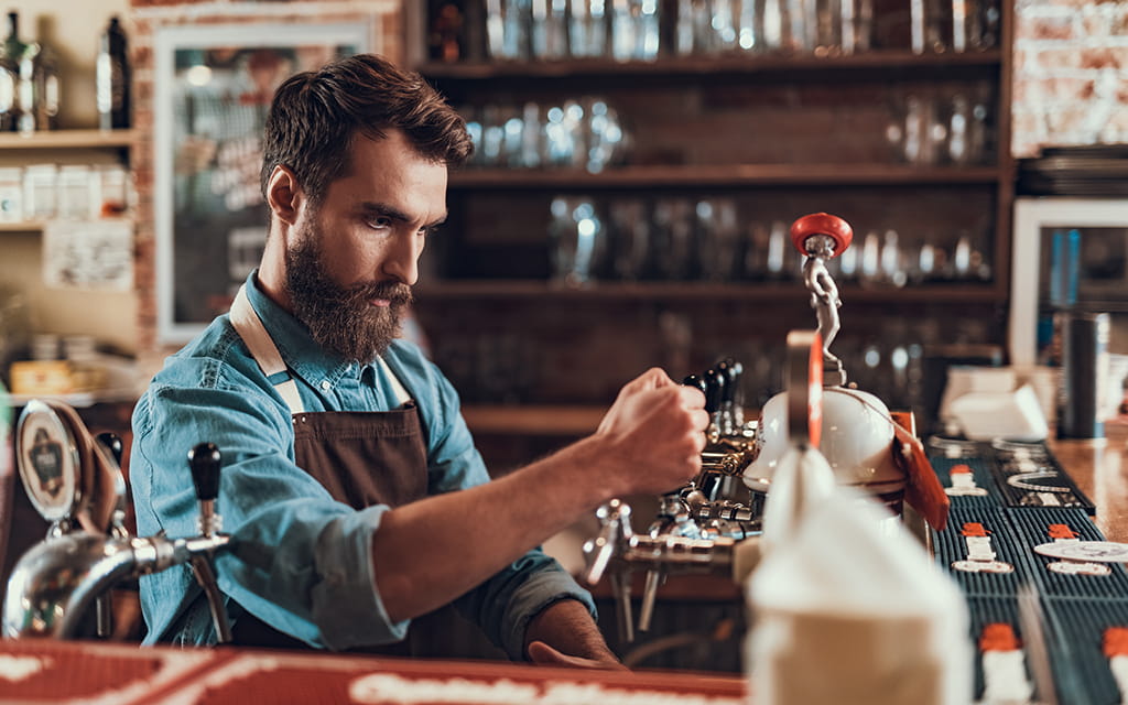 Barkeeper steht hinter der Bar und zapft ein Bier Barkeeper steht hinter der Bar und zapft ein Bier