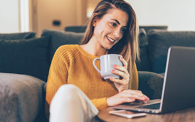 Dame sitzt vor dem Sofa auf dem Boden und arbeitet an einem Laptop