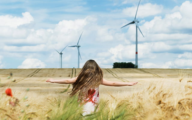 Junge Frau steht in einem Feld mit Windrädern im Hintergrund