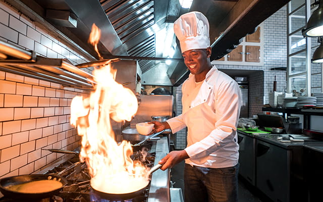 Junger Koch flambiert Essen in einem Restaurant