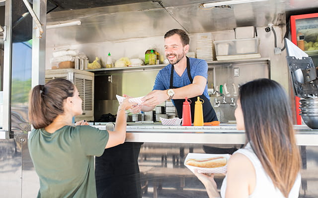 Zwei junge Frauen kaufen sich an einem Imbisswagen etwas zu Essen Zwei junge Frauen kaufen sich an einem Imbisswagen etwas zu Essen